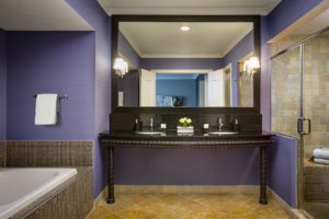 Guest room bathroom with purple walls, a brown double sink vanity, a large soaking tub and walk in shower