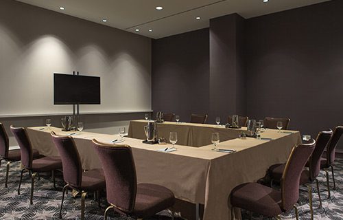 Boardroom setup with black tables, white chairs and water glasses in front of screen at Hotel Chicago Downtown, Autograph Collection