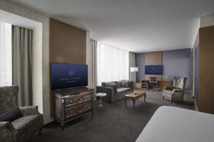 Bedroom with grey carpet and furniture in front of two tvs at Hotel Chicago Downtown, Autograph Collection