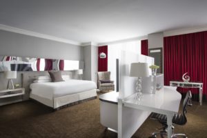 Bed with white linens and red curtains in front of white desk near chairs at Hotel Chicago Downtown, Autograph Collection