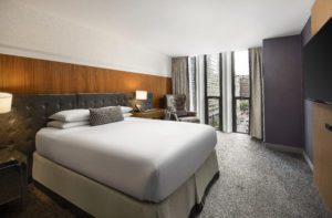 Large bed with white linens in front of tv overlooking buildings with black walls at Hotel Chicago Downtown, Autograph Collection