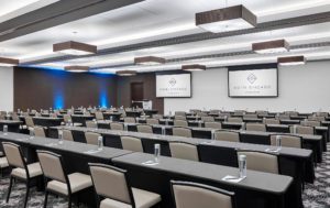 A modern hotel conference room in downtown Chicago with rows of tables, bottled water, and large screens—perfect for events and meetings.