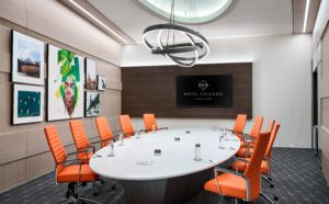 Boardroom in downtown Chicago with a white modern table and orange office chairs set with water bottles, pens and paper