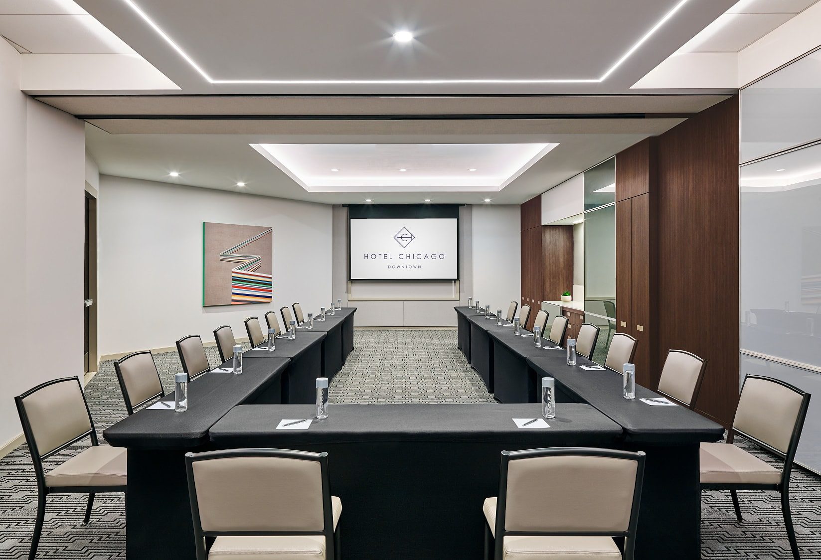 Meeting room in downtown Chicago, set in a u shaped setting with black linened tables, water bottles and pen and paper at Hotel Chicago Downtown, Autograph Collection