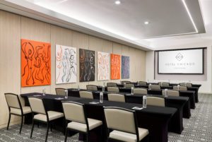 Black tables in front of white chairs with water bottles on them and modern art on walls at Hotel Chicago Downtown, Autograph Collection