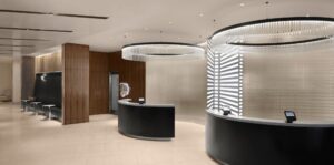 Modern hotel lobby in downtown with two curved desks, wood paneling, benches, and gallery-style circular ceiling lights. Sleek, minimalist design.